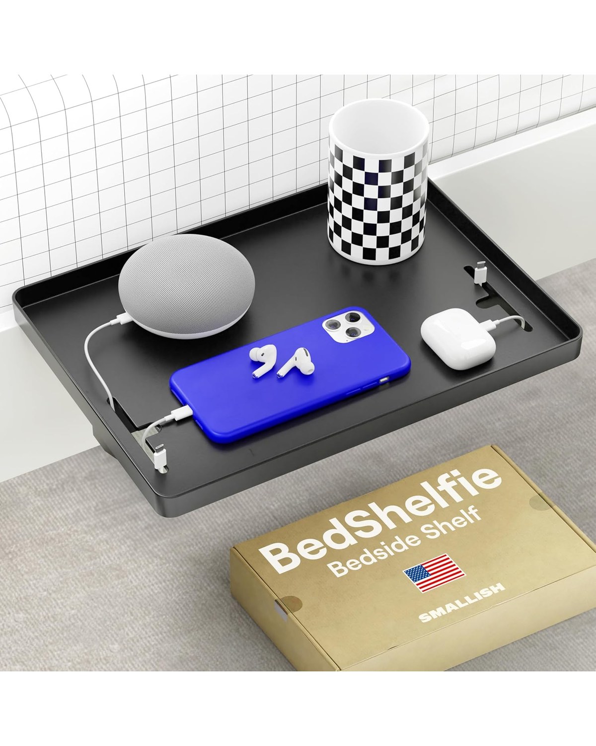 A minimalist black metal bedside shelf clipped to the side rail of a dorm-style bed frame, holding a phone, water bottle, and AirPods case at arm's reach.
