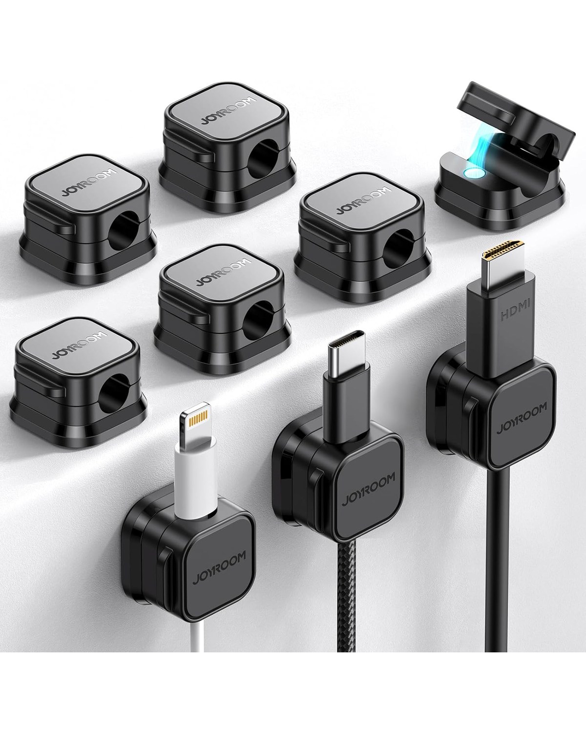 Nine small magnetic cable clips lined along the back edge of a white desk, each holding a different cable — phone charger, USB-C, laptop — flat against the surface with no dangling cords visible.