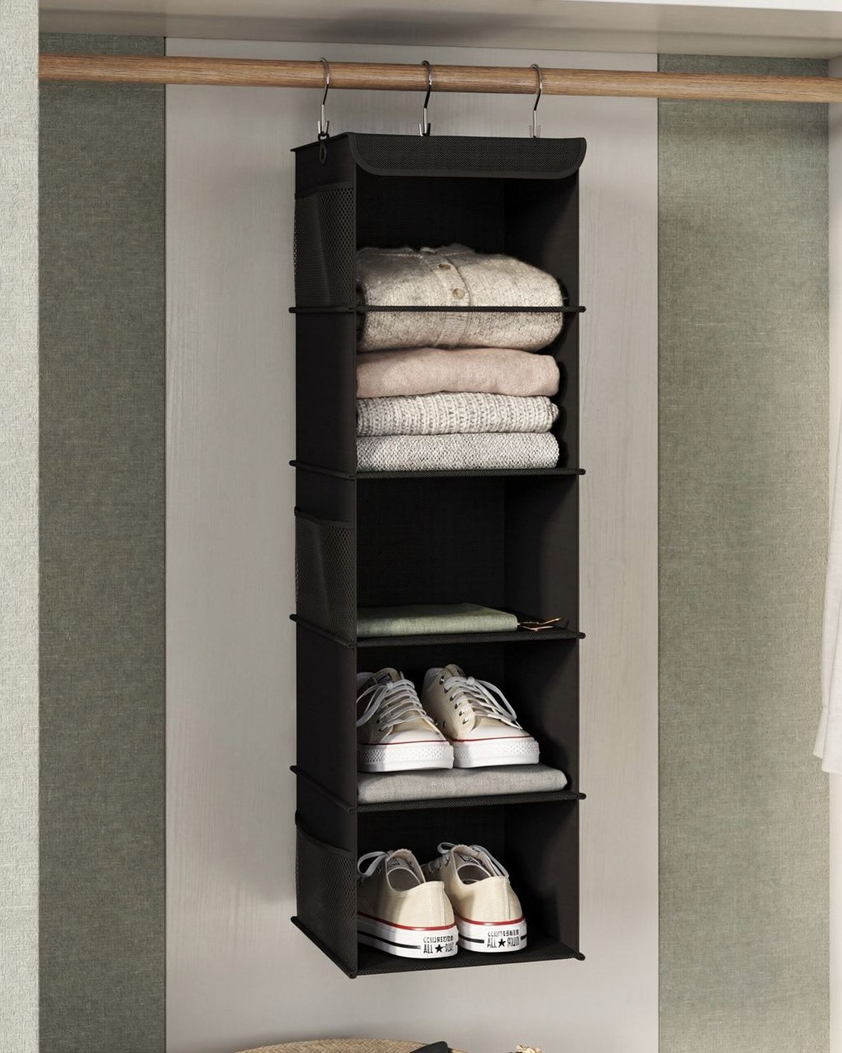 A black 5-shelf fabric organizer hanging from a closet rod, each shelf stacked with folded sweaters and shoes.