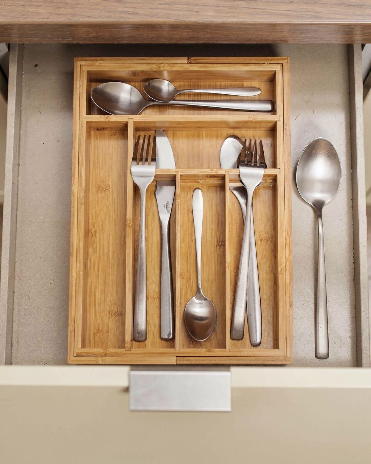 A natural bamboo cutlery tray with angled compartments that slides open to expand and fill the width of a kitchen drawer.