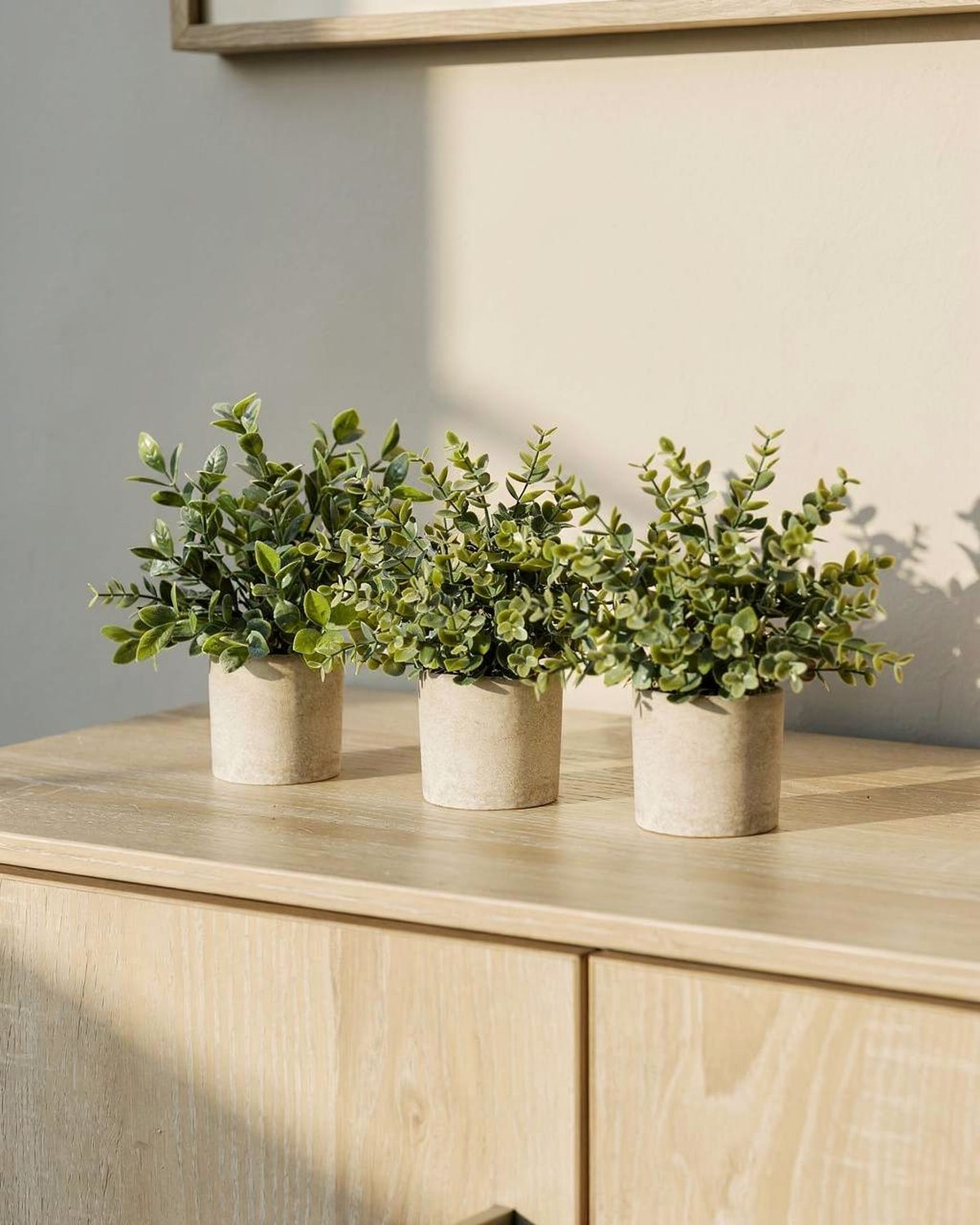 Three small white pots holding lifelike faux eucalyptus and greenery, sized for a shelf, console or side table.