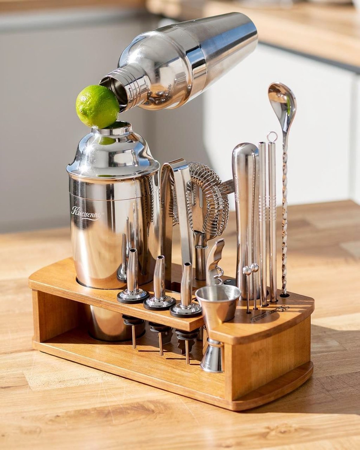 A stainless cocktail shaker and matching bar tools arranged on a freestanding rack, ready on a counter.