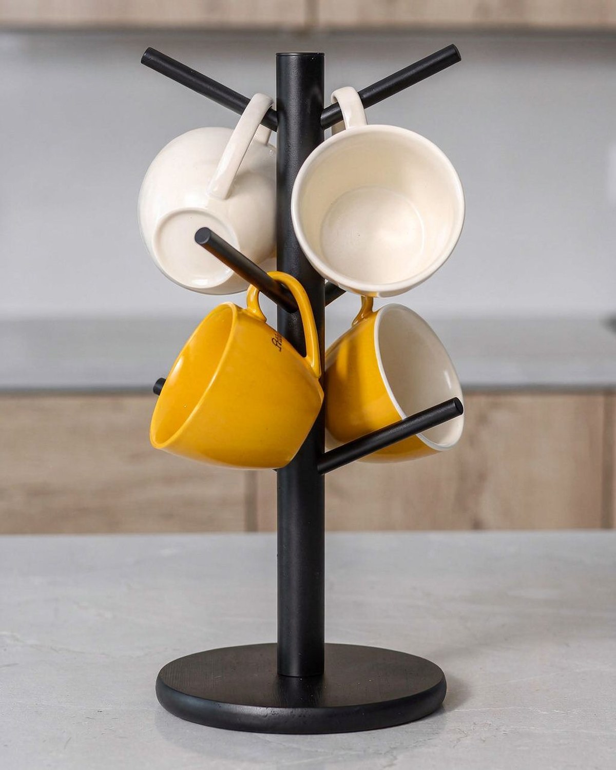 A black metal countertop tree with six curved hooks holding hanging mugs around a slim central post.