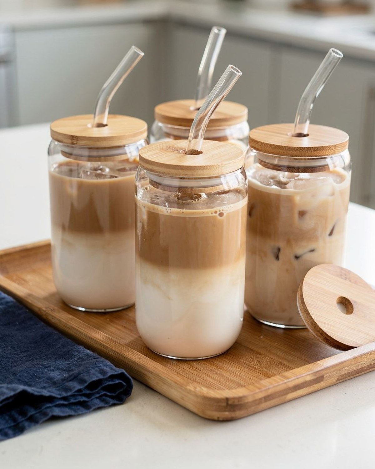 A set of clear 16-ounce glass tumblers with natural bamboo lids and glass straws, filled with iced coffee.