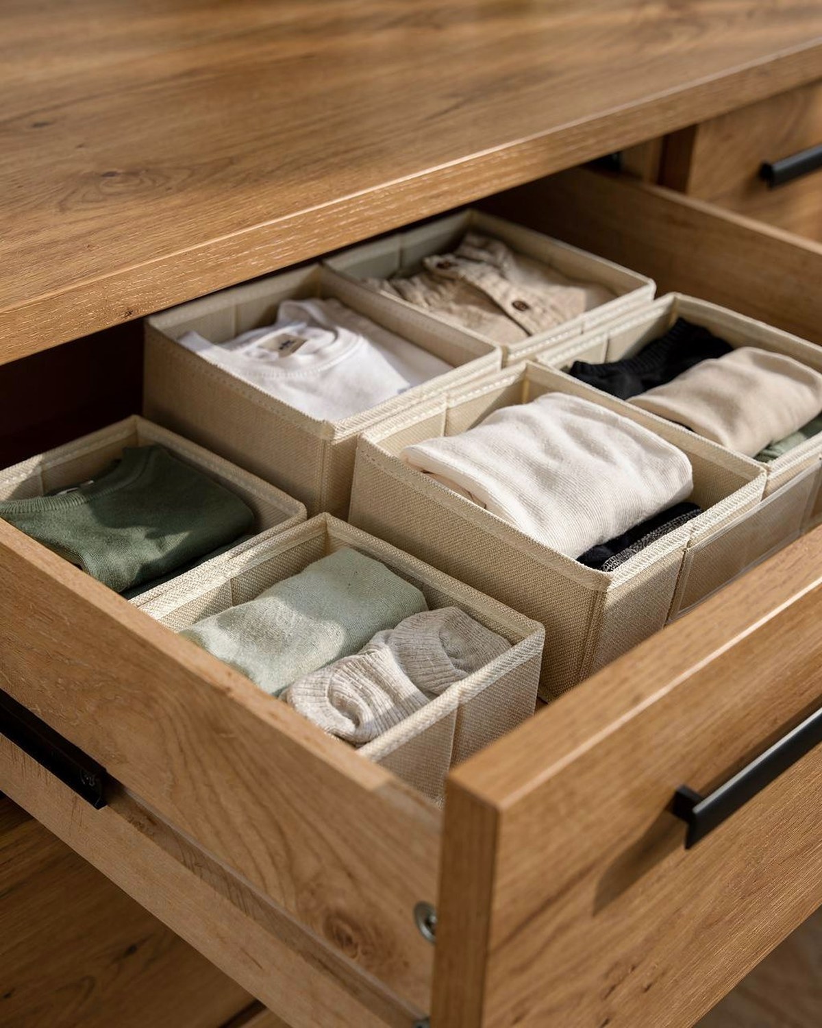 A set of beige foldable fabric drawer bins of mixed sizes nested inside an open dresser drawer, separating socks, underwear, and tops.