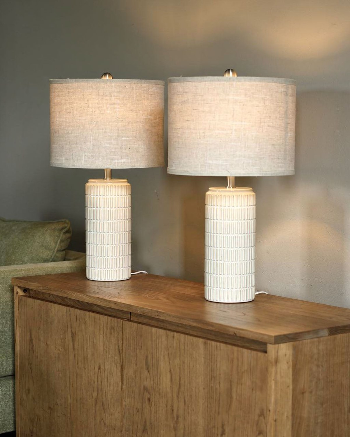 A matched pair of white textured ceramic table lamps with neutral drum shades, flanking a sofa or console.
