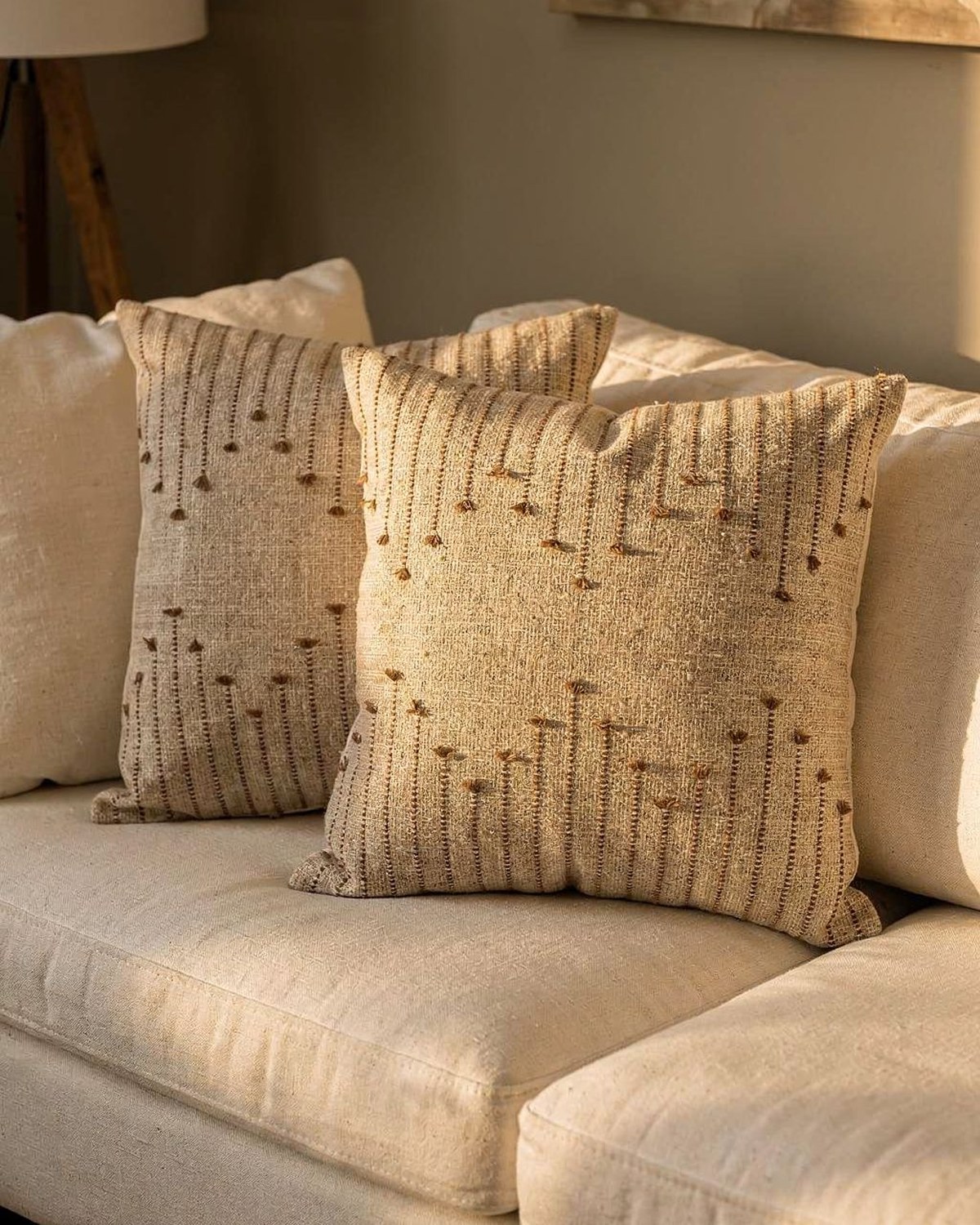 Two textured woven pillow covers in beige and brown with a subtle tufted geometric pattern, layered against a cream set.