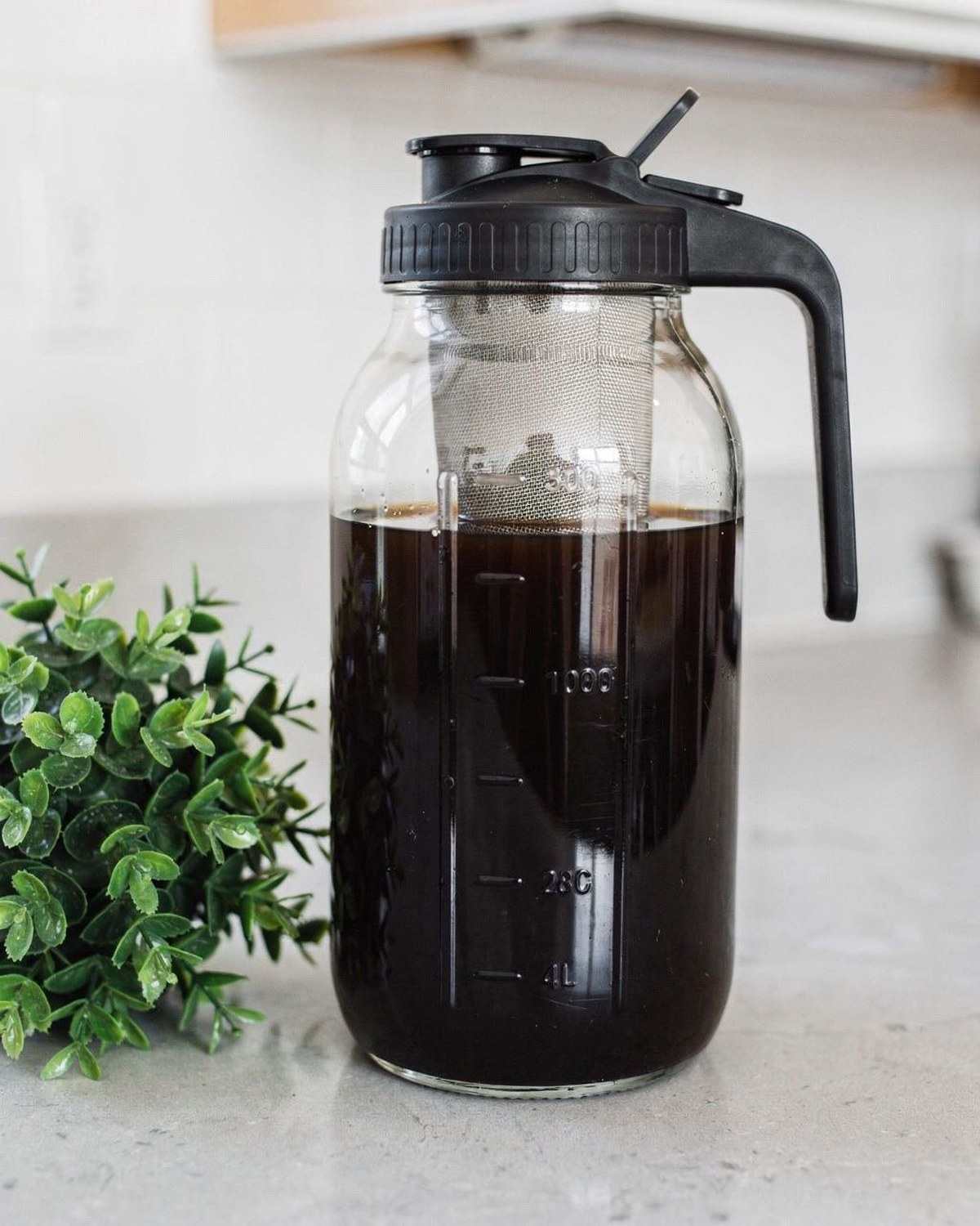 A large 64-ounce glass mason-jar pitcher with a fine stainless mesh filter insert, filled with dark cold-brew coffee.