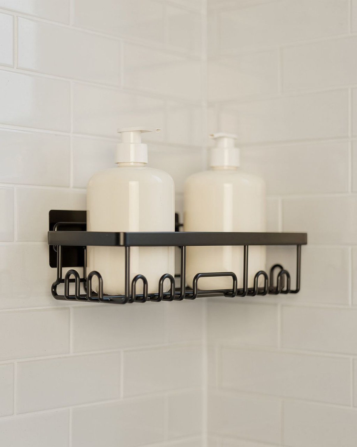 A black no-drill adhesive shower organizer set with two tiered shelf baskets plus hooks and a toothbrush and soap holder, mounted on tile holding bottles.