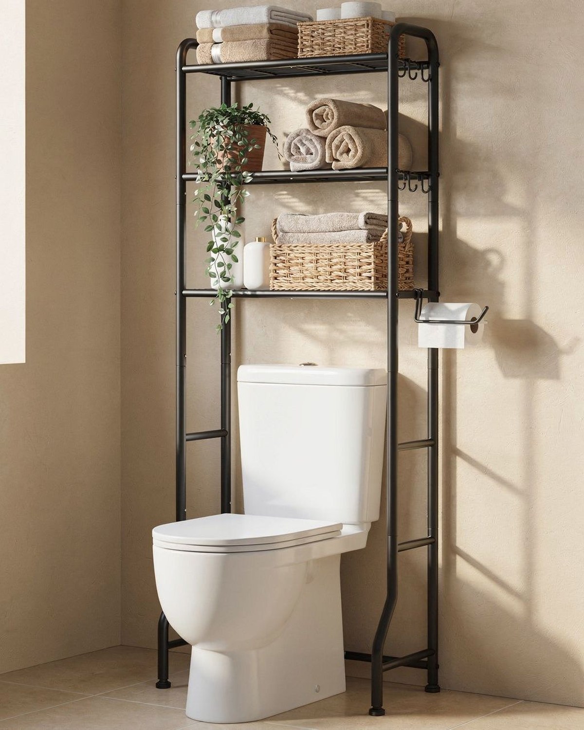 A slim black metal freestanding shelf that straddles the toilet tank with open tiers holding towels, baskets, and plants.