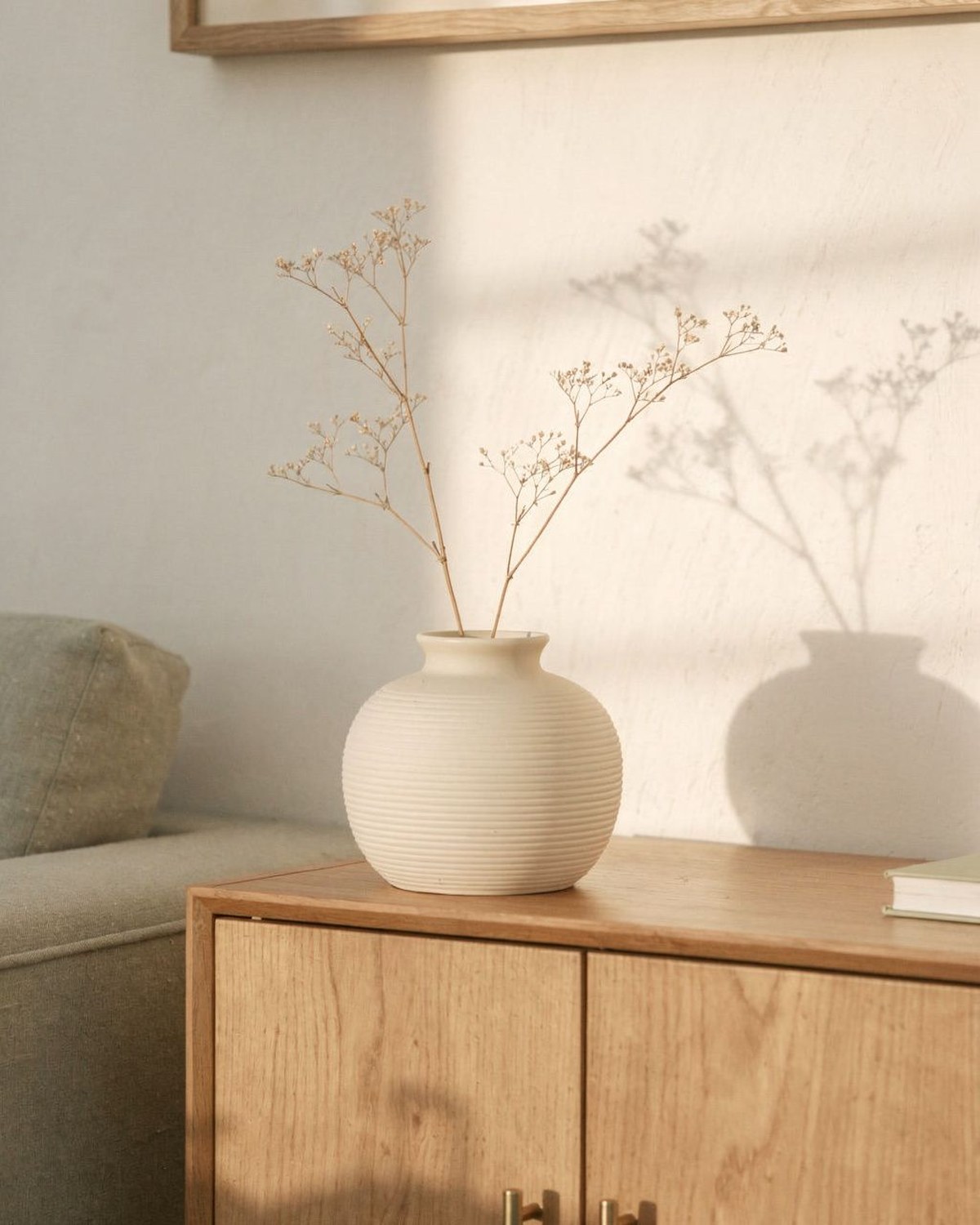 A matte cream farmhouse-style ceramic vase with a rounded body and narrow neck, styled with a few stems.