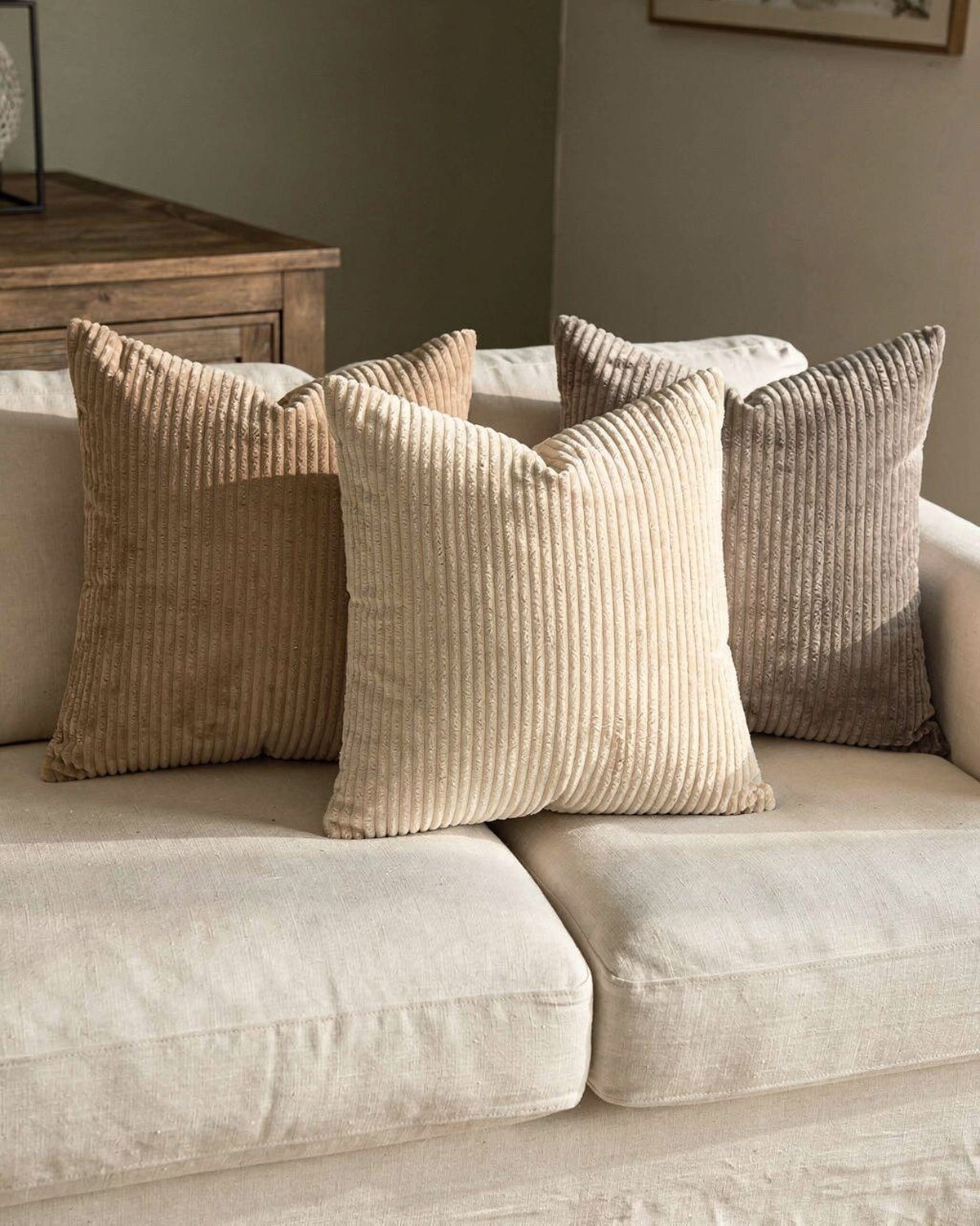 Four soft corduroy pillow covers in cream and warm neutral tones arranged on a light sofa.