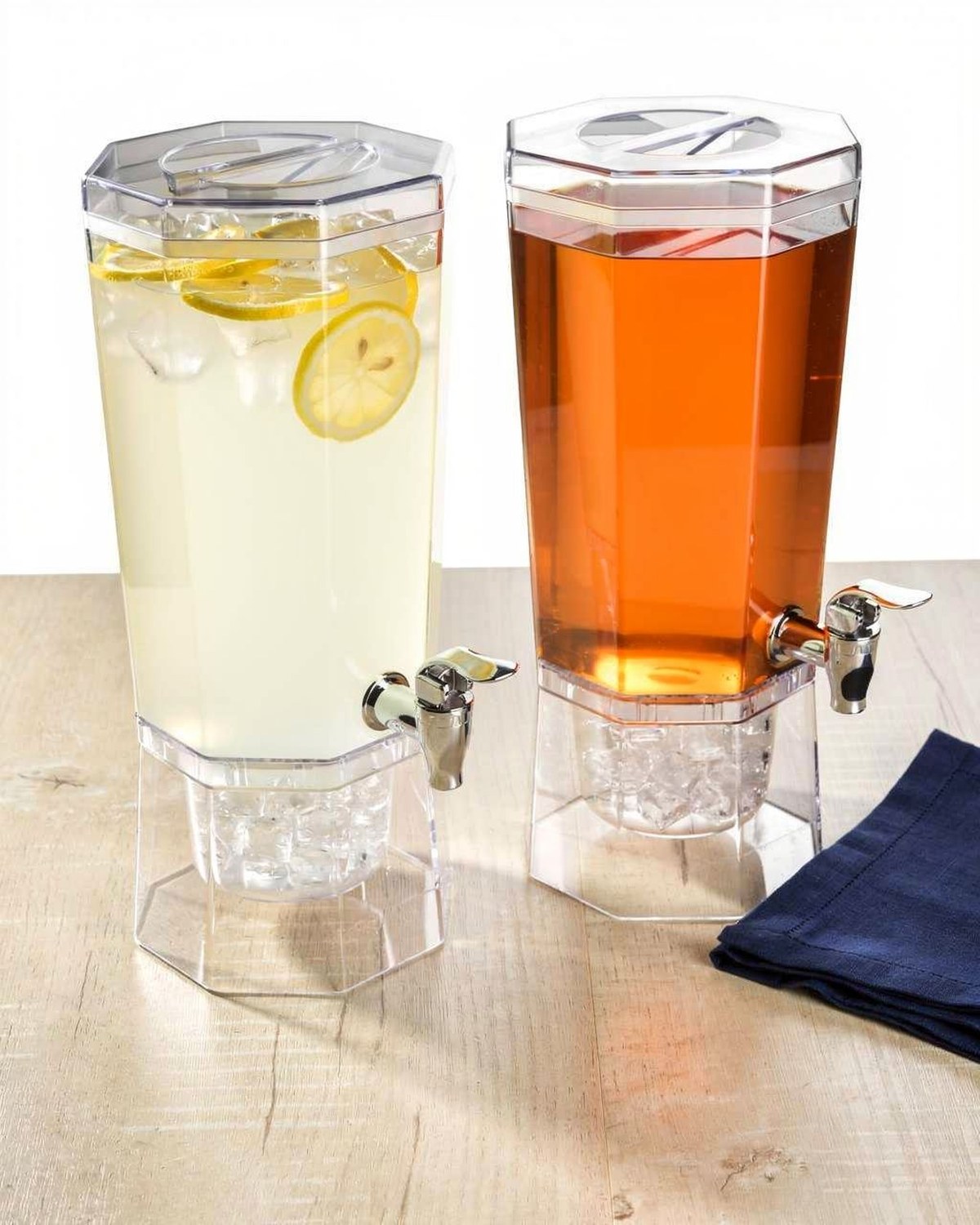 Two clear glass beverage dispensers with spigots, filled with lemonade and infused water for a party.