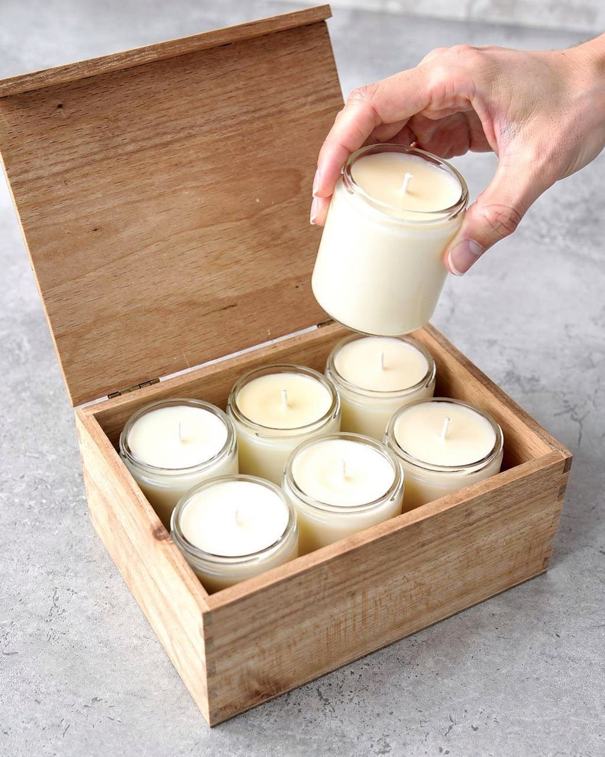 Six small soy candles in a coordinated gift box, lids off to show pastel-toned wax, styled as a present.