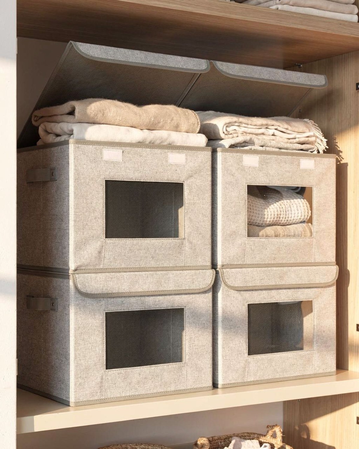 Four labeled fabric storage boxes with lids stacked on a closet top shelf
