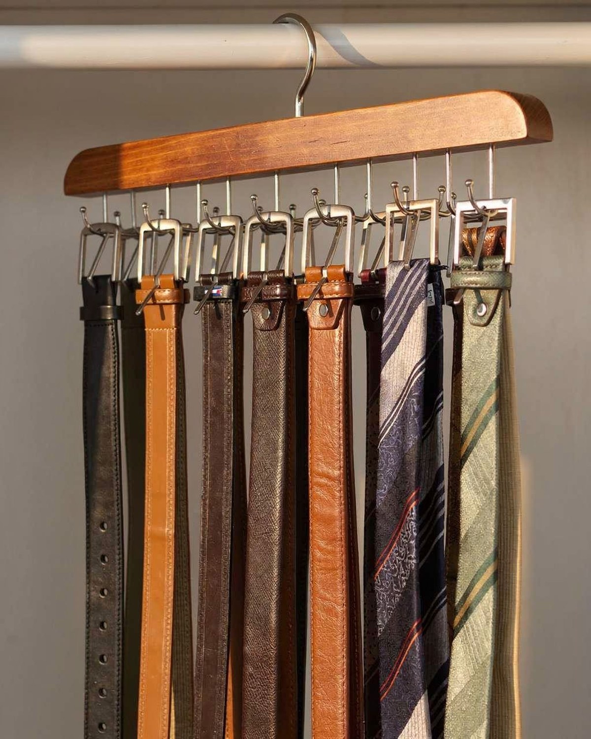 Wooden rotating hanger holding belts and ties on a closet rod