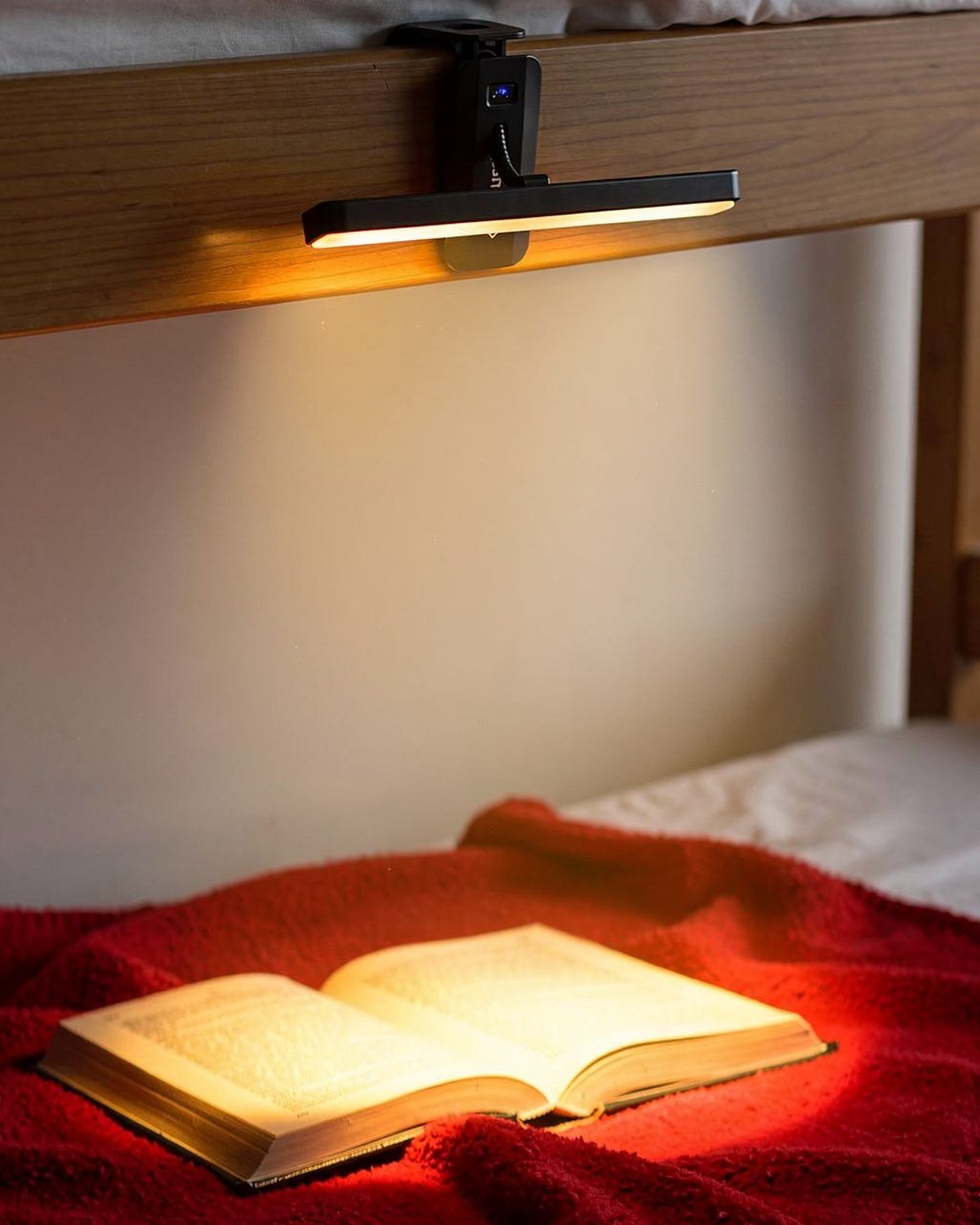 Rechargeable clip-on reading light with a warm amber glow beside an open book in a dark dorm